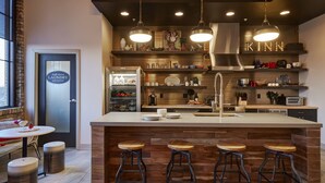 A modern kitchen with a central island, bar stools, a self-serve laundry sign, and various kitchen appliances. - Kinn Guesthouse Bay View (Milwaukee)