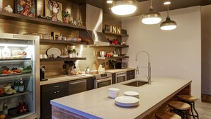 A modern kitchen with a central island, bar stools, stainless steel appliances, and decorative items on shelves. - Kinn Guesthouse Bay View (Milwaukee)
