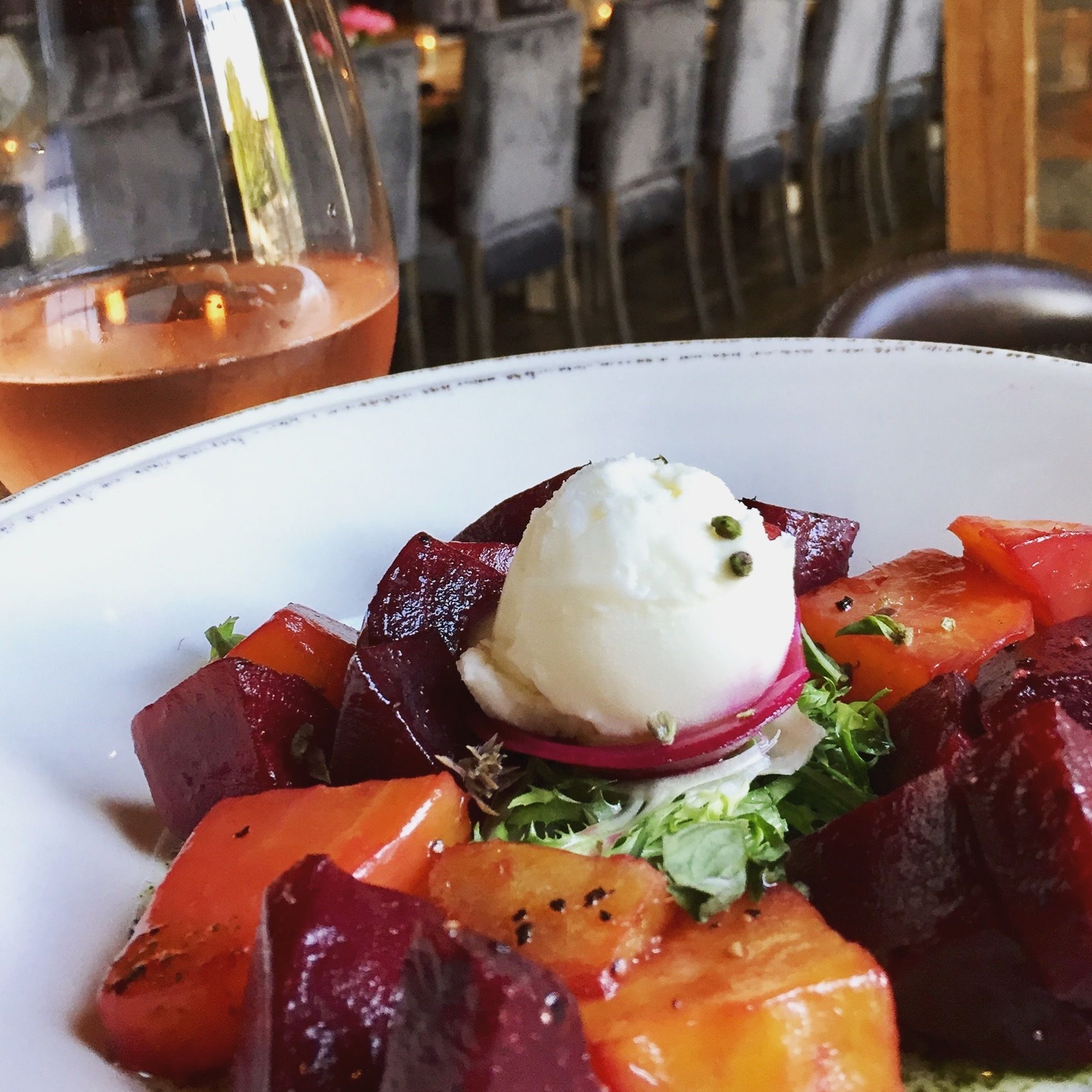 A plate of food with a scoop of white cream on top, surrounded by beetroot and carrot slices, and garnished with green leaves.