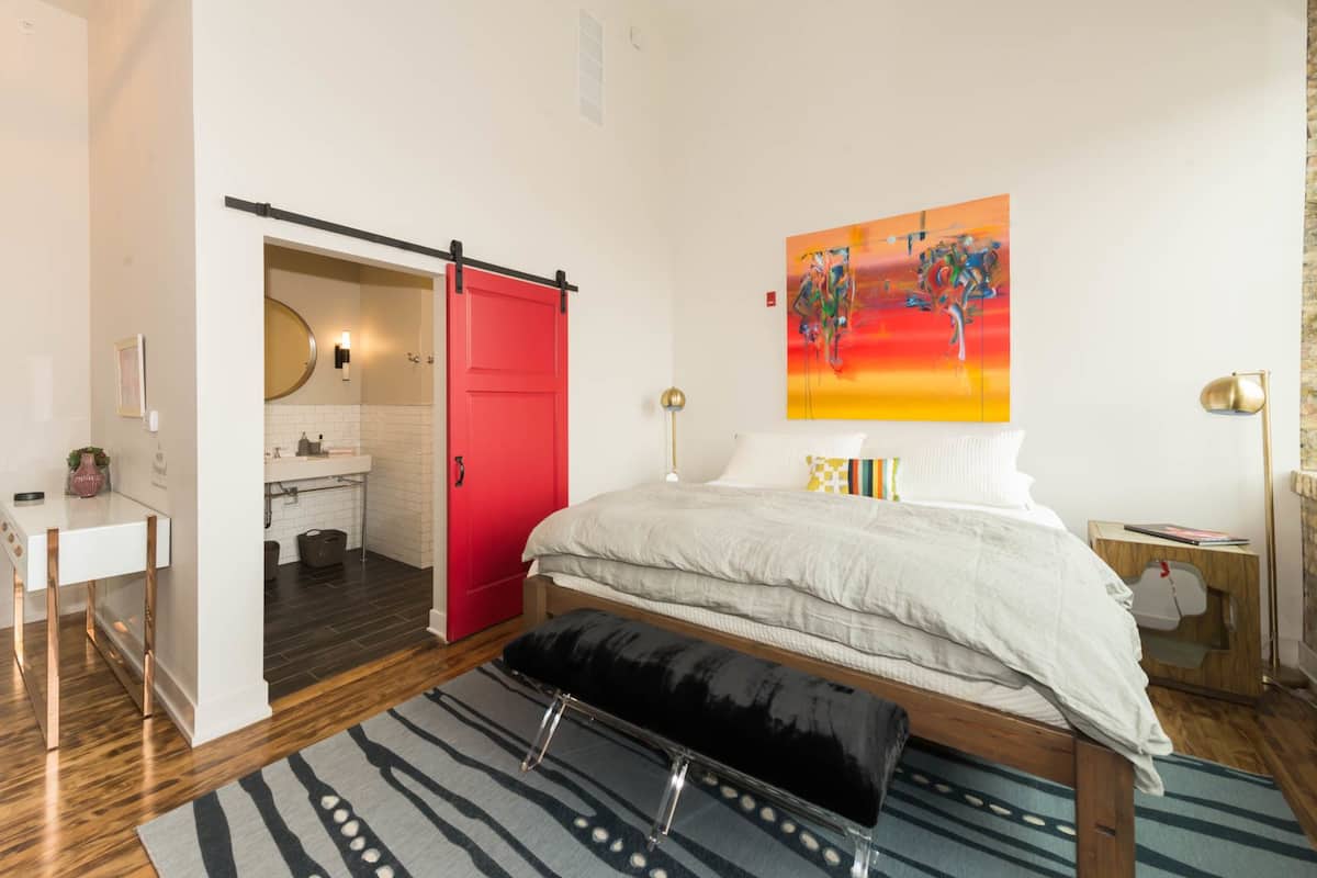 Ein Schlafzimmer mit Bett, einer roten Tür, einem Badezimmer und einem Bild an der Wand.