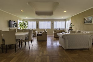 A spacious living room with a dining area, large windows, and a ceiling with recessed lighting.