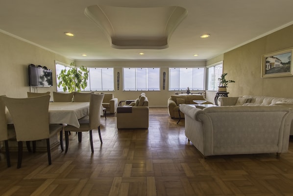 A spacious living room with a dining area, large windows, and a ceiling with recessed lighting.