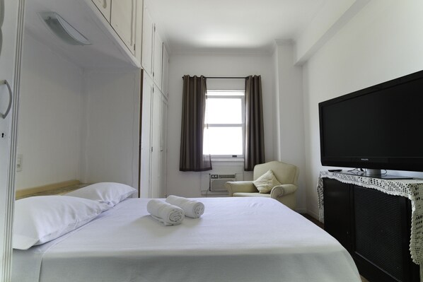 A hotel room with a bed, a television, a chair, and a window with curtains.
