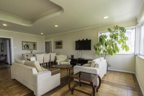 A spacious living room with a sofa, armchairs, a coffee table, and a television.