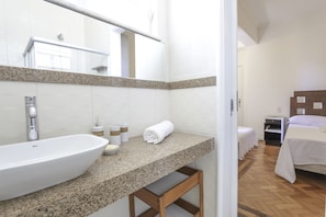 A hotel bathroom with a large sink, a mirror, and a wooden bench.