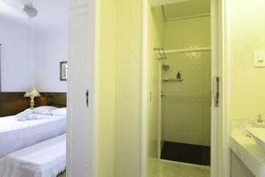 A hotel room with a bed, a bedside lamp, a shower area, and a bathroom with a sink.