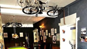 A cozy room with a pool table, a red sofa, wooden benches, and bicycles hanging from the ceiling. - Strathcarron Hotel (Strathcarron)