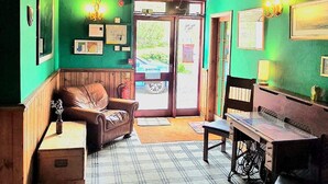 A cozy room with a plaid carpet, a wooden bench, a sewing machine, and a green wall with framed pictures. - Strathcarron Hotel (Strathcarron)