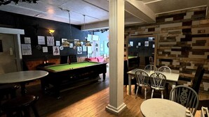 A billiards room with tables and chairs, a pool table, and a wooden wall with framed pictures. - Strathcarron Hotel (Strathcarron)