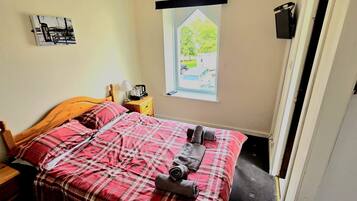 A bedroom with a bed, a nightstand, a lamp, a window with a view of a tree and a car, and a wall-mounted TV.