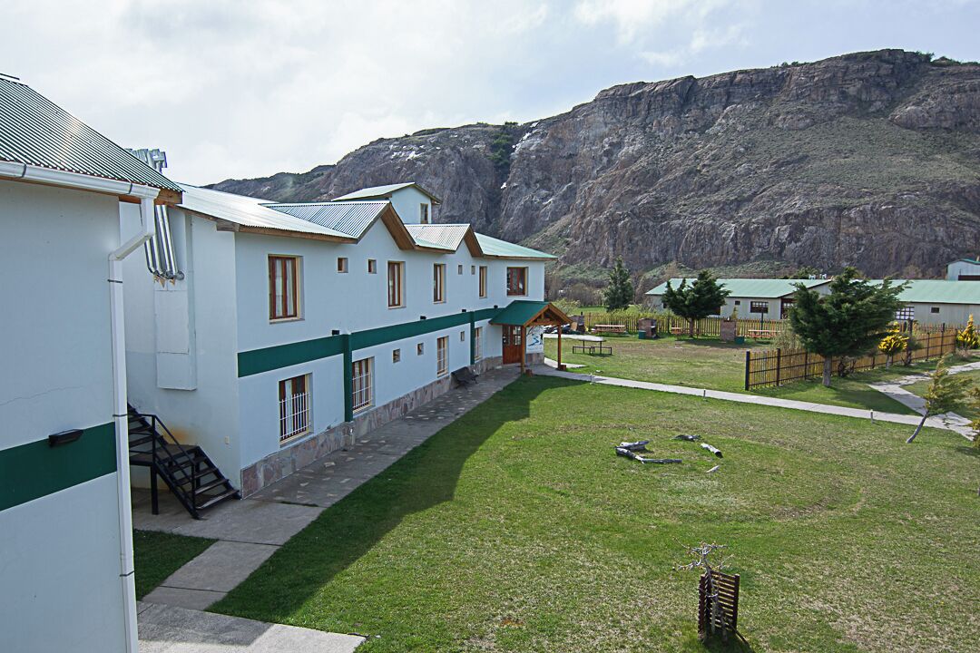 A building with a green and white exterior, a staircase leading to the entrance, and a grassy courtyard with a mountain in the background.