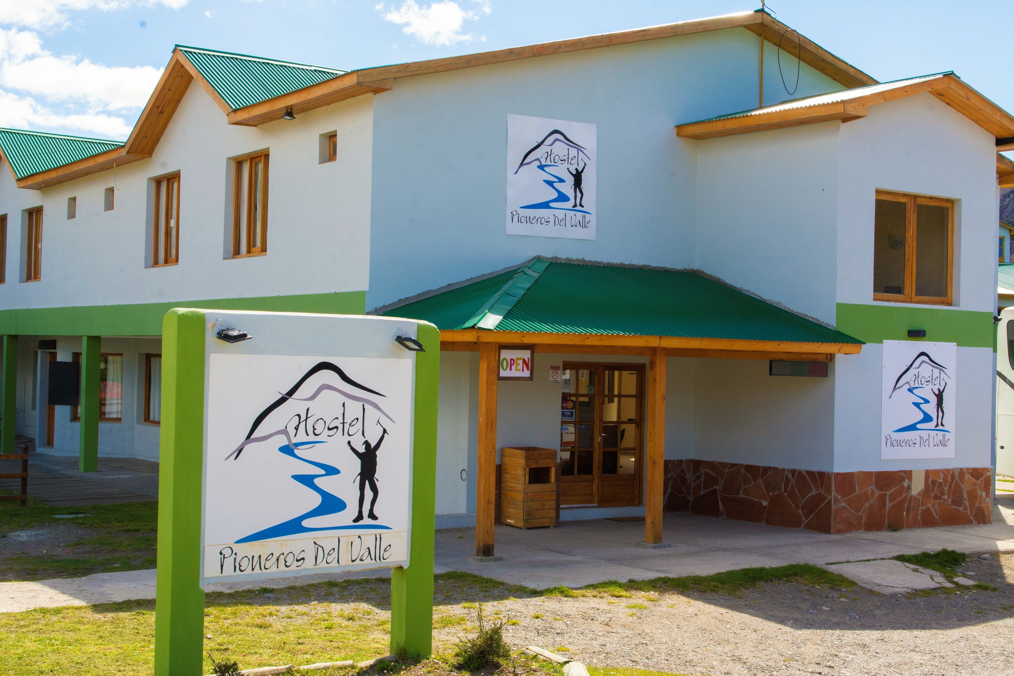 A two-story building with a green roof and a sign indicating it is a hostel named "Pioneros Del Valle".