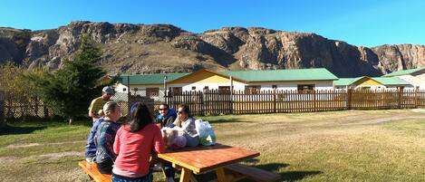 Un grupo de personas sentadas en una mesa de picnic de madera en un área con césped, con montañas al fondo.