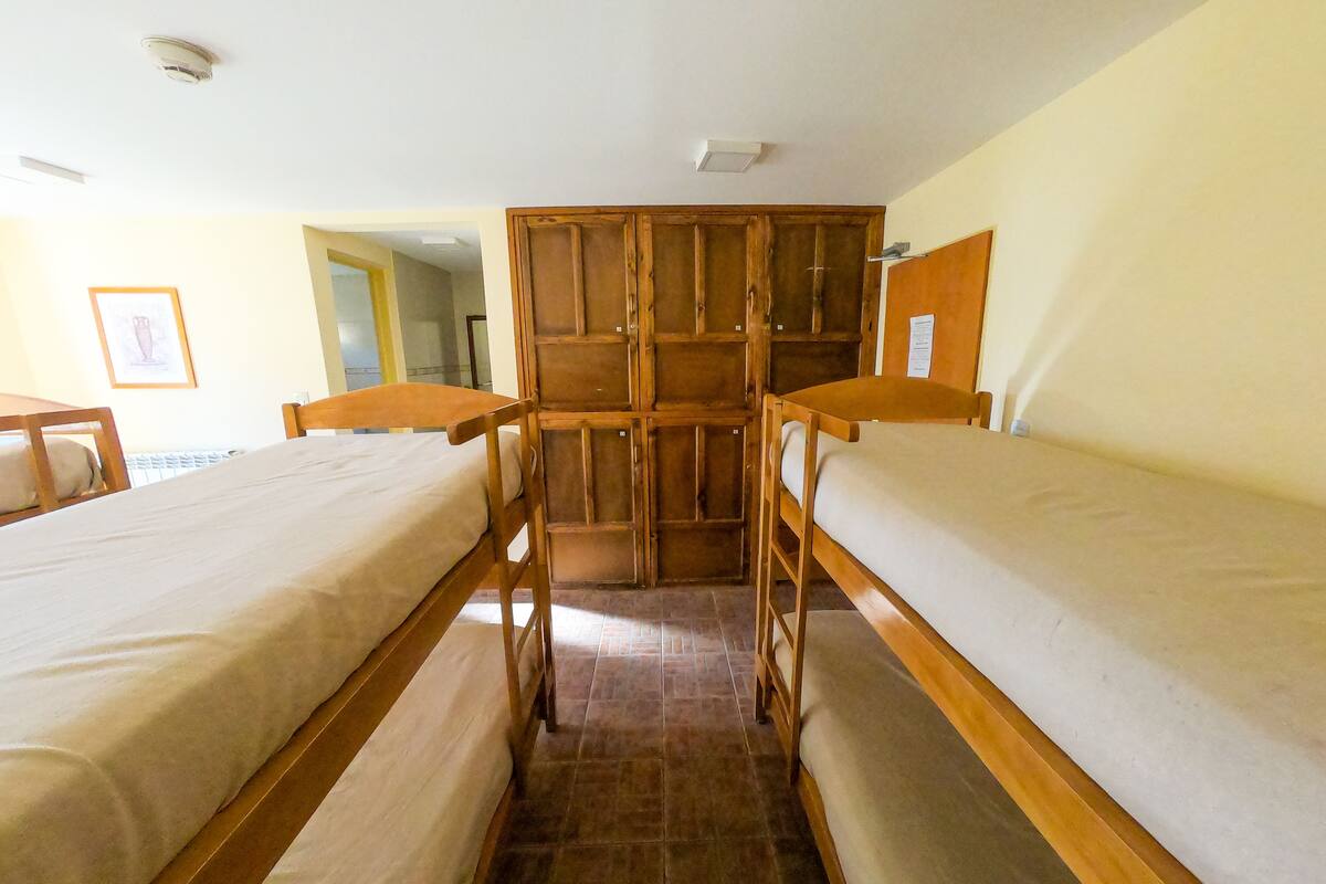 Ein Schlafsaalzimmer mit zwei hölzernen Etagenbetten, einem Holzschrank und einem Fliesenboden.