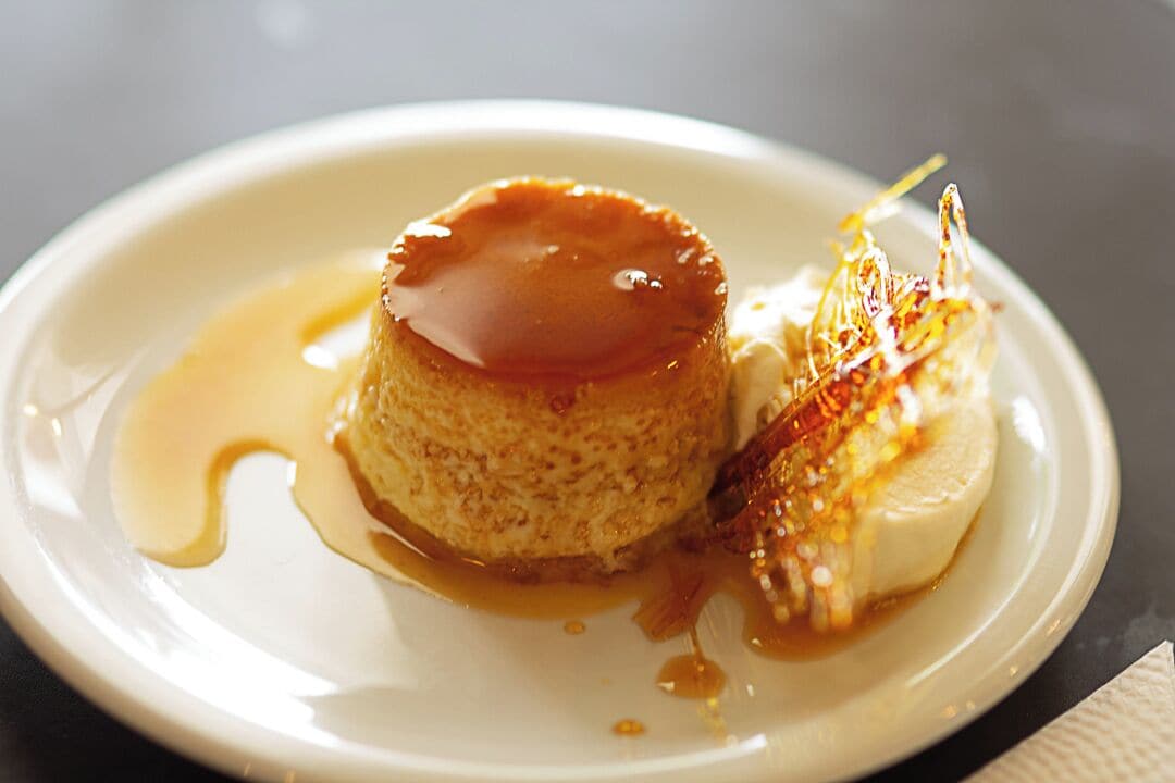 A dessert plate with a caramel flan and a scoop of ice cream, both drizzled with caramel sauce.
