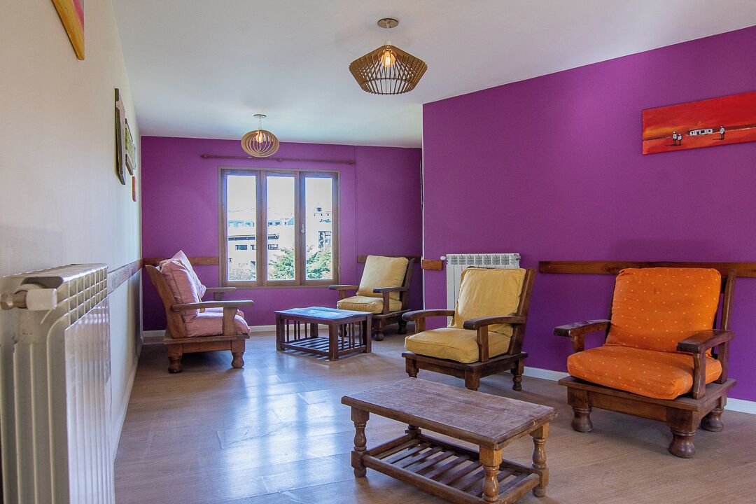 Una sala de estar con paredes moradas, muebles de madera y una ventana que ofrece vistas a edificios.