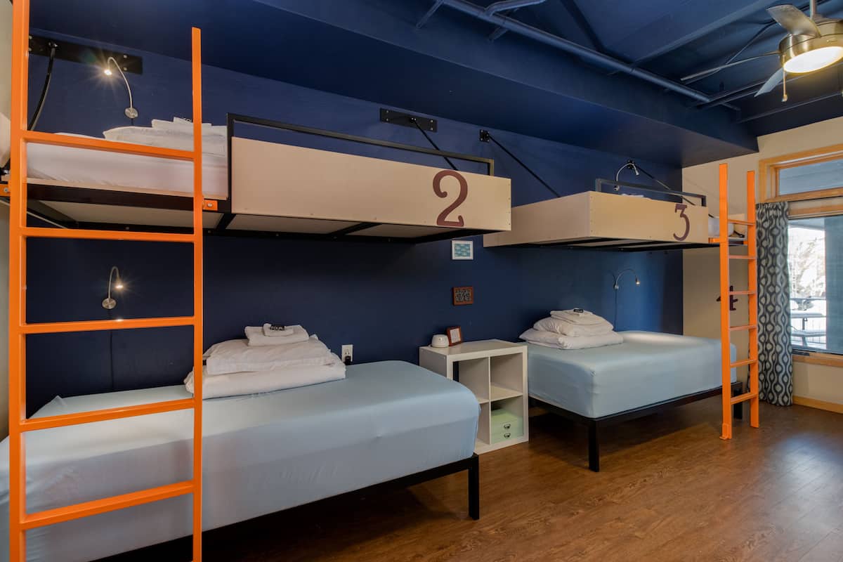 A dormitory room with bunk beds labeled 2 and 3, a small white nightstand, and a window with curtains.