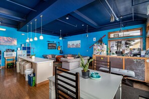 Um espaço de estar moderno com uma parede azul de destaque, área de jantar com mesa e cadeiras, sofá e cozinha com bancada e eletrodomésticos.