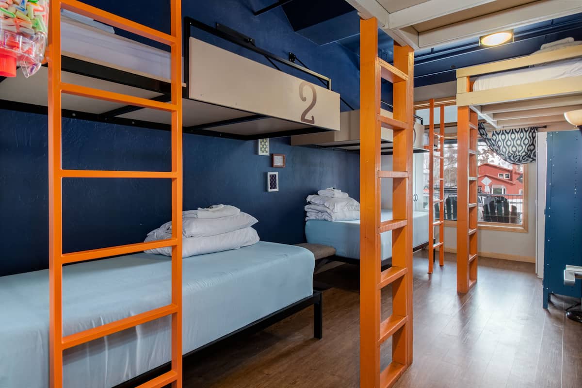 A dormitory room with bunk beds, a number '2' sign, a window with a view of houses, and a basketball hoop.