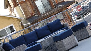 A wooden building with a balcony, a wicker sofa with blue cushions, and a mountainous backdrop. - The Bunkhouse - Hostel (Minturn)