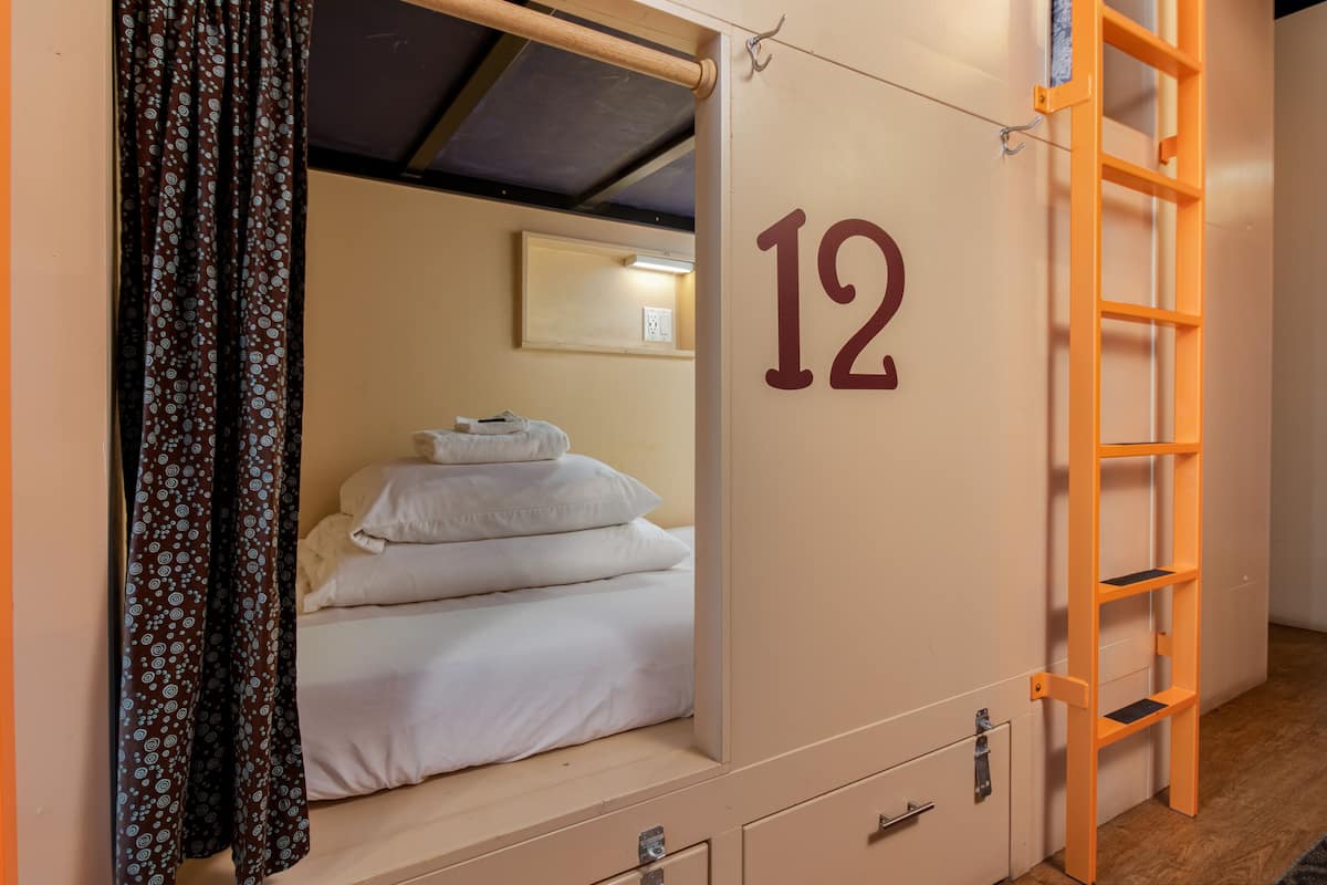 A single room with a bunk bed, a number '12' on the wall, a small desk, and a ladder.
