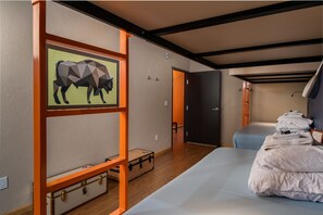 Quarto de hotel com cama, mala, quadro emoldurado e um banco.