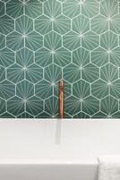 A bathroom with a green geometric tile backsplash and a copper faucet.