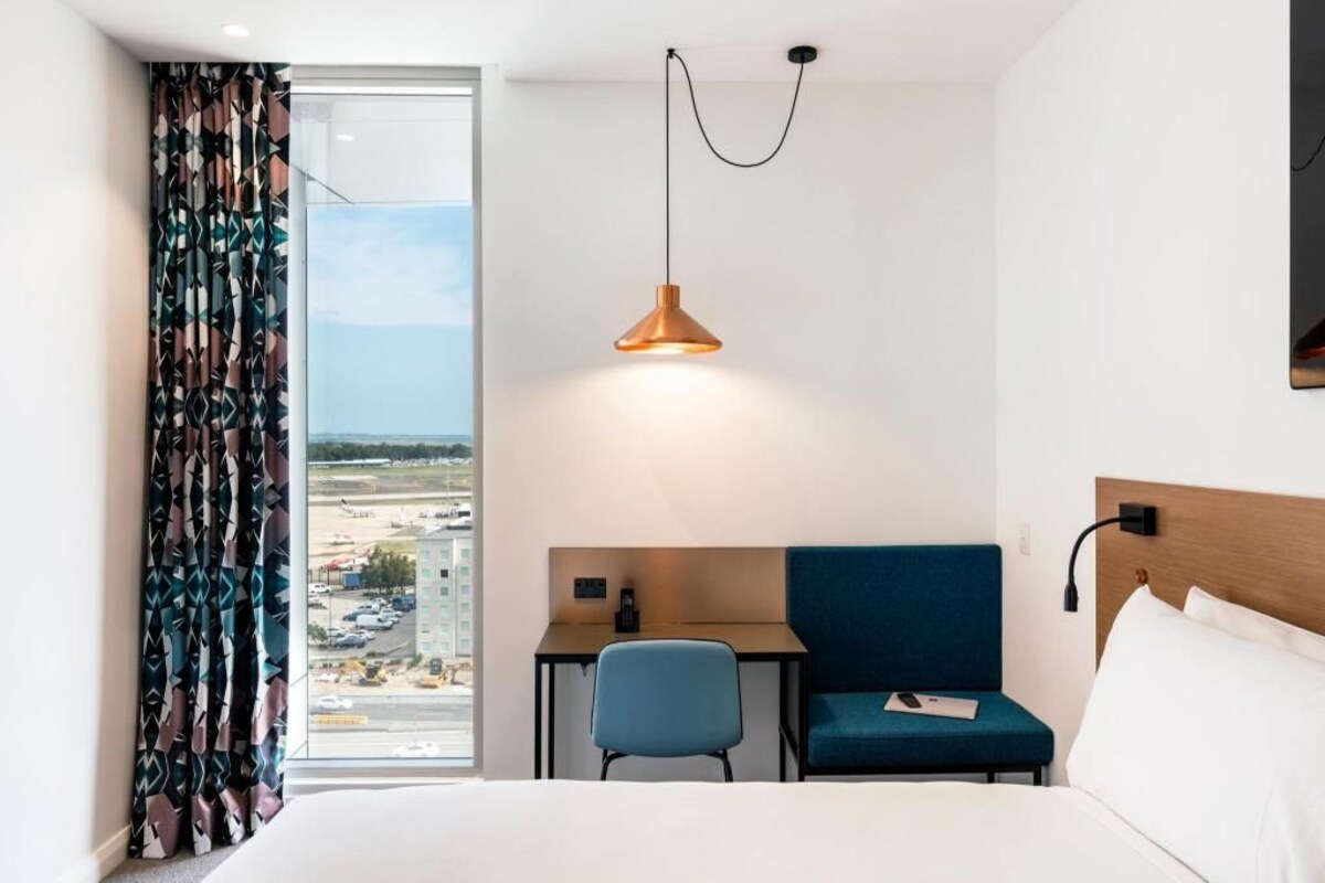 Habitación de hotel con cama, escritorio, silla, lámpara colgante y vistas al exterior.