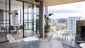 Un balcón interior moderno con vistas a la ciudad, que cuenta con techo de madera, paredes de vidrio y sillas de metal.