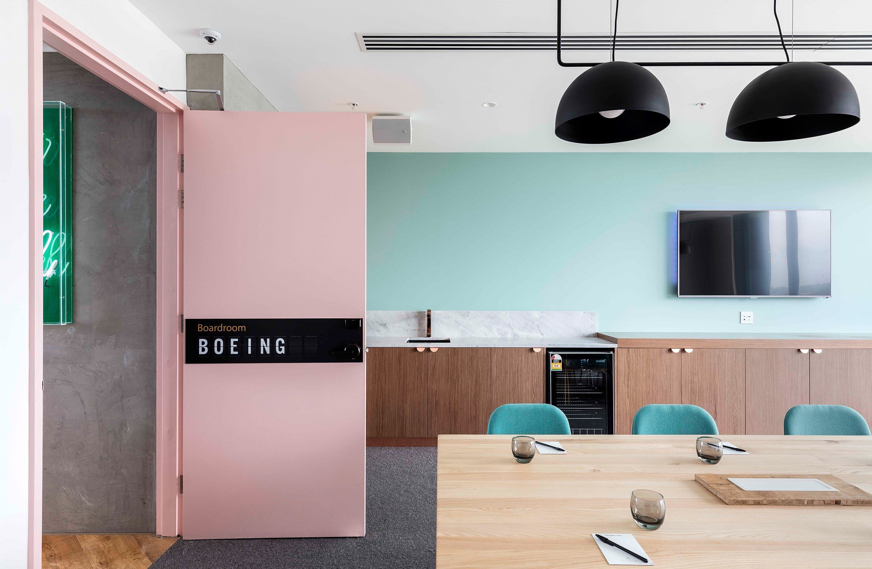 Una cocina moderna con un refrigerador rosa, paredes verde azulado y una mesa de comedor de madera.