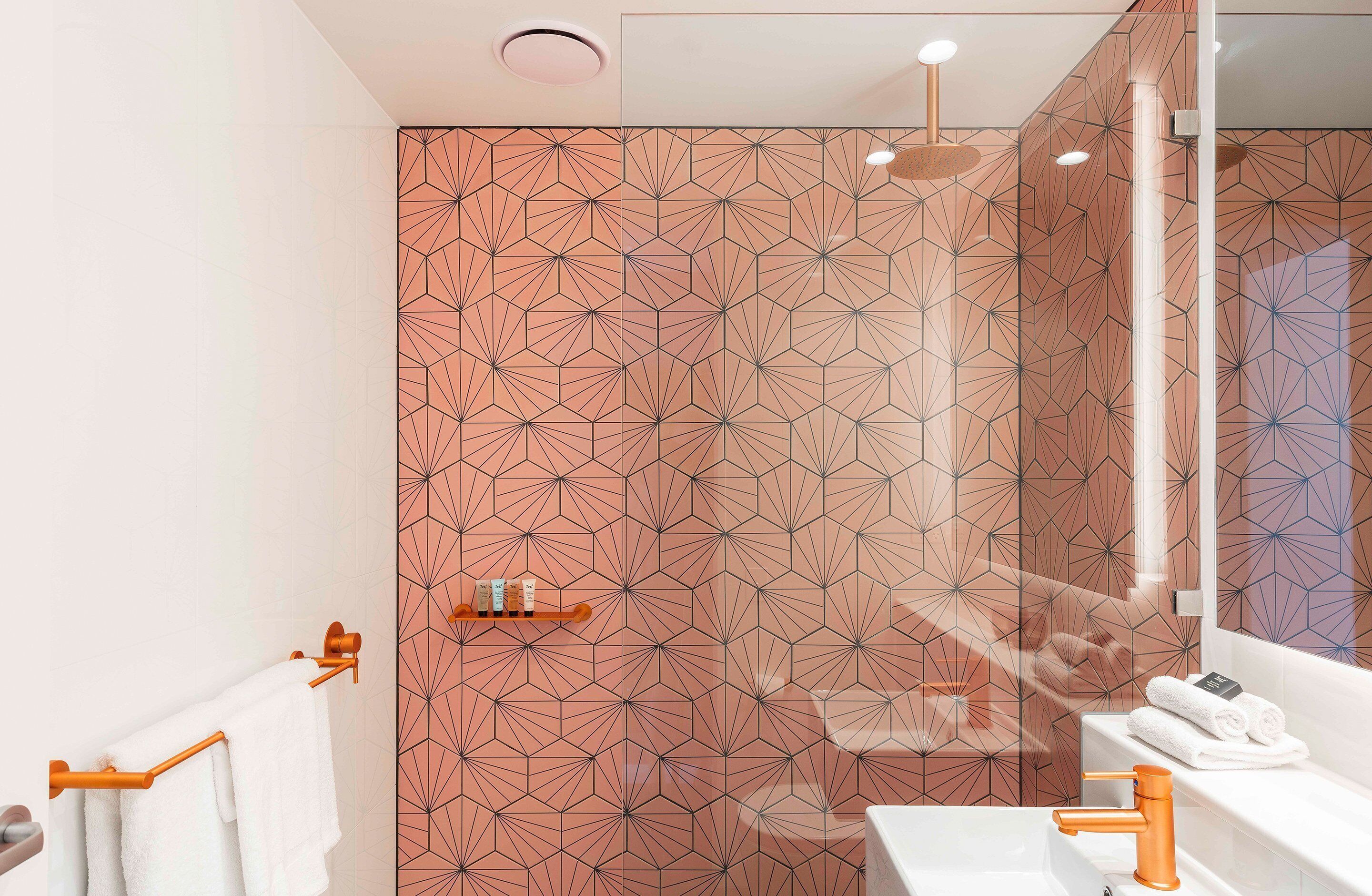 A modern bathroom with a geometric patterned wall, a white sink, and a wooden towel rack.