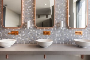 A bathroom with three white vessel sinks, a hexagonal tiled backsplash, and three rectangular mirrors with copper frames.