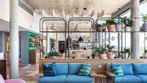 Un vestíbulo amplio con un sofá azul, mesas de madera y plantas en macetas.