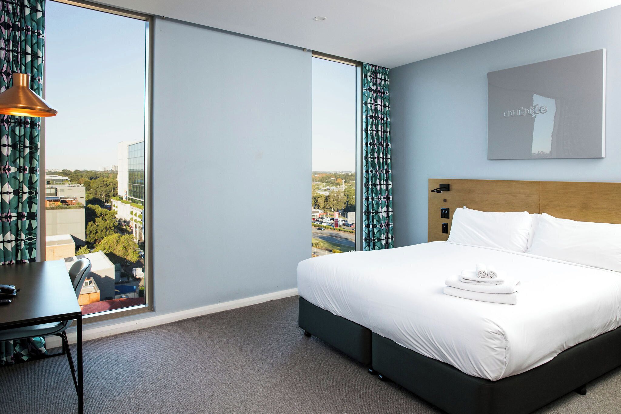 A hotel room with a large bed, a desk, and a view of the city.