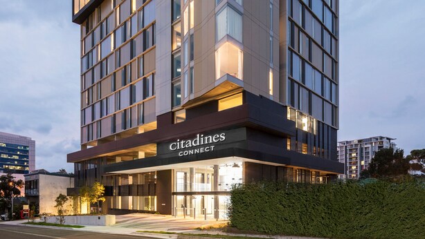Un moderno edificio de hotel con un llamativo letrero 'Citadines CONNECT', amplias ventanas y una entrada bien iluminada.