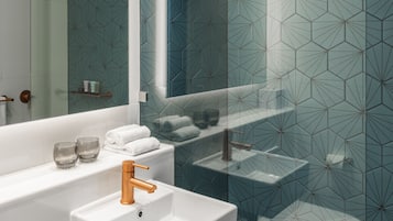 Un baño moderno con un lavamanos blanco, una cabina de ducha de vidrio y un revestimiento de pared con patrón geométrico.