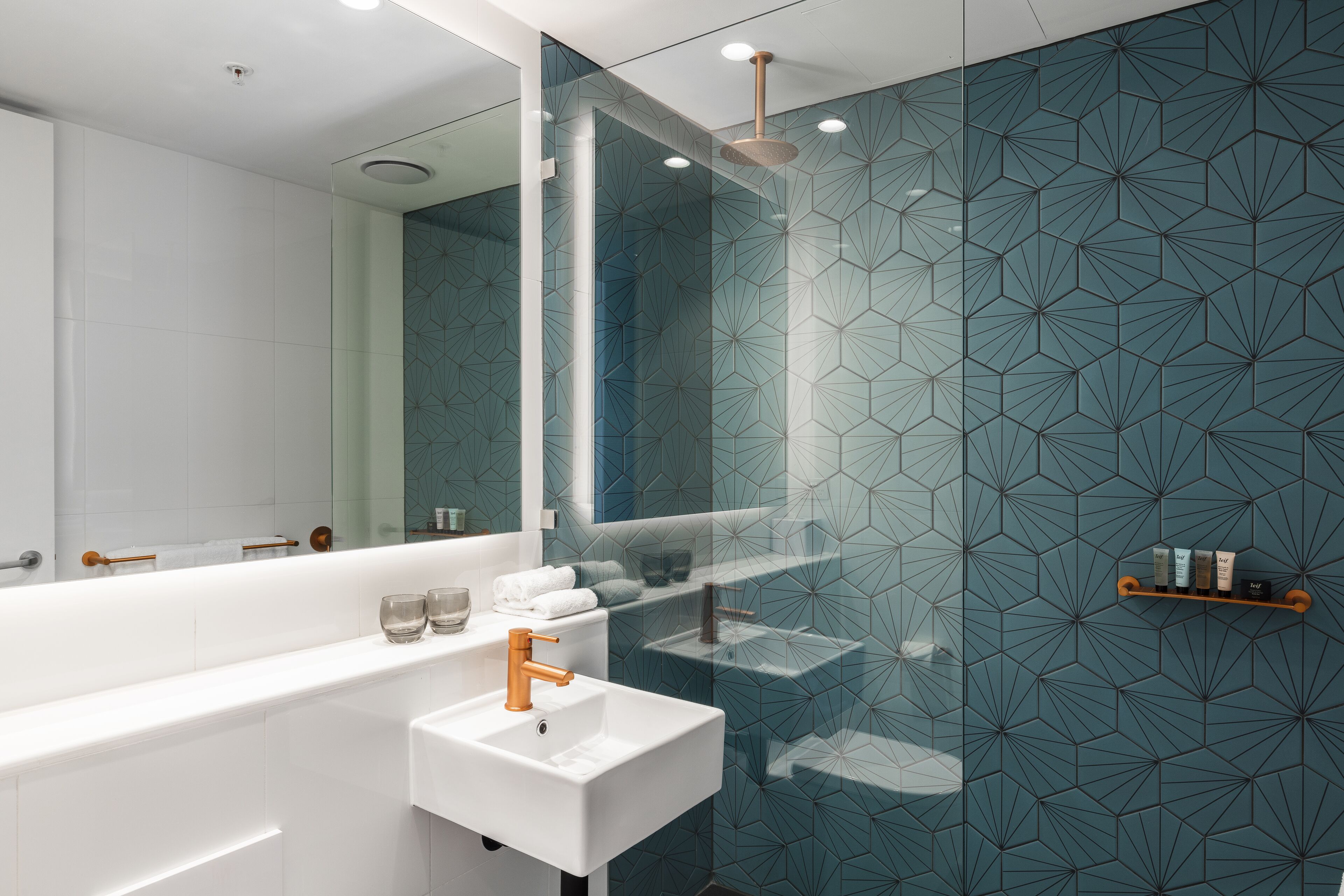A modern bathroom with a white sink, a mirror, and a shower area.