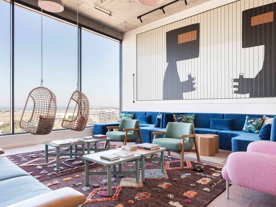 A modern living room with a large window, blue sofa, hanging chairs, and a colorful rug.