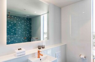 A modern bathroom with a large mirror, two sinks, a shower, and a window providing natural light.