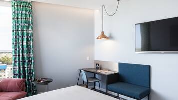 Habitación de hotel moderna con cama, escritorio, silla, televisor y vista a la ciudad.