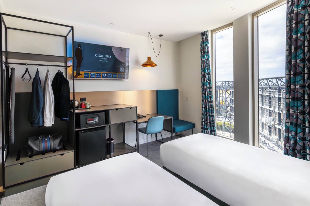 A hotel room with two beds, a desk, a chair, a TV, and a wardrobe.