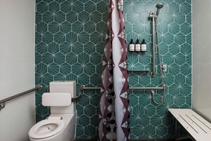 Un baño con un diseño de azulejos geométricos, inodoro blanco, ducha con cabezal de ducha de mano y un banco.