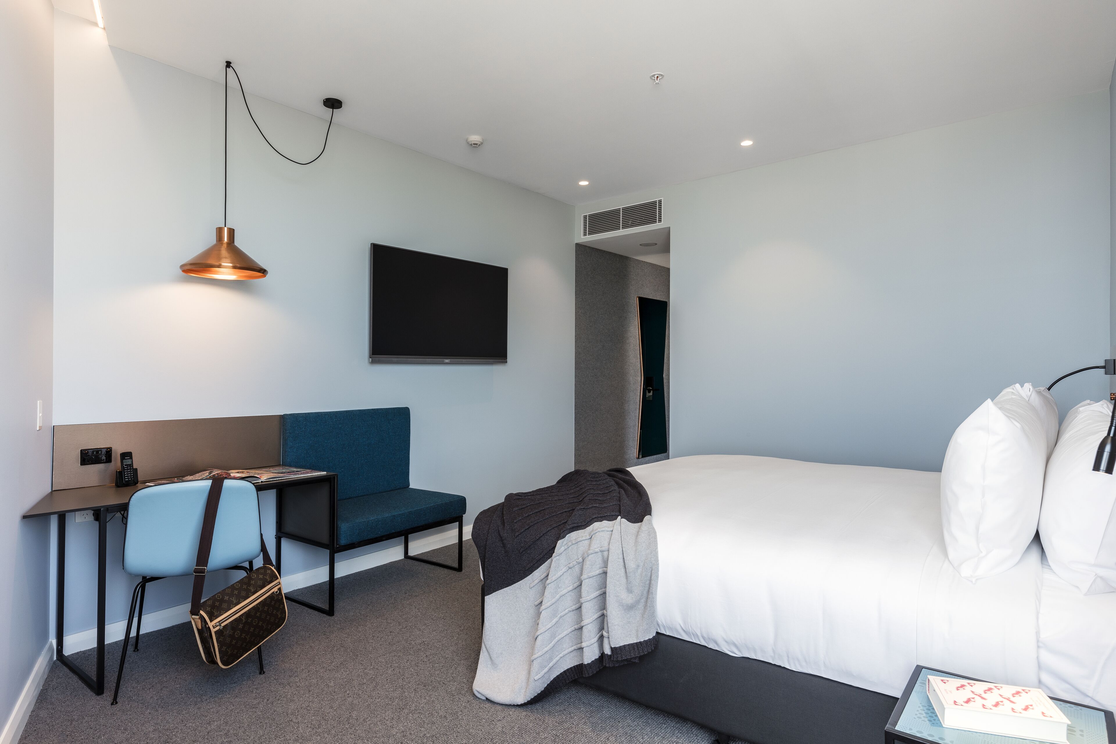 Quarto de hotel moderno com uma cama, uma mesa de escritório com cadeira, uma televisão e um espaço de estar.