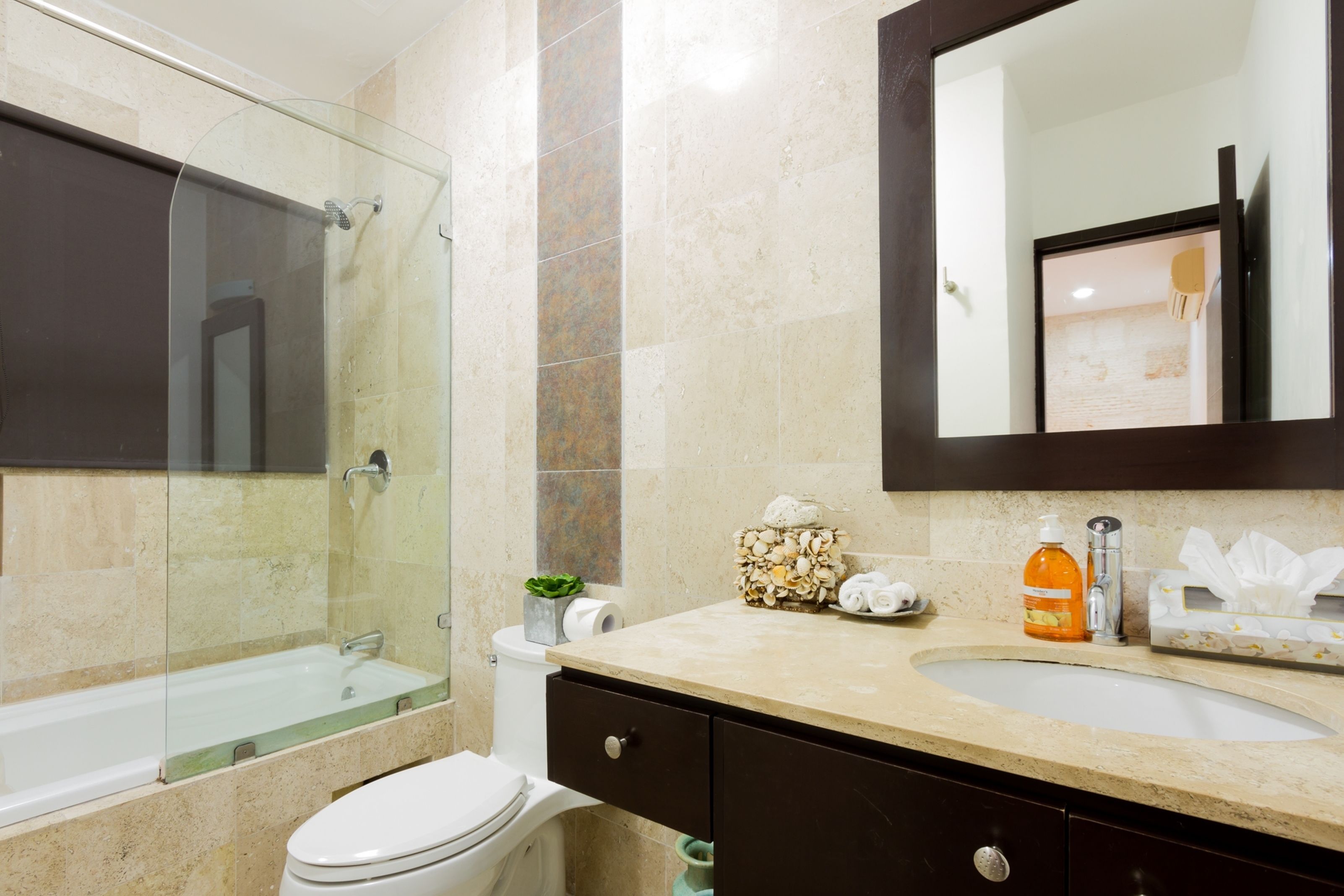 A modern bathroom with a glass-enclosed shower, a white toilet, a beige sink, and a dark wooden cabinet.