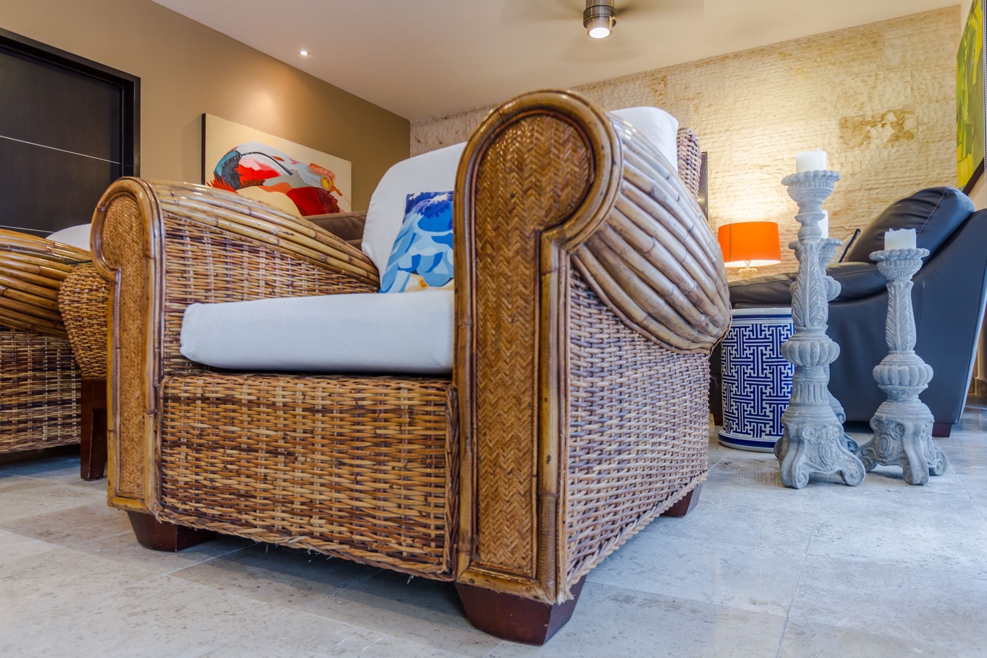 Un canapé en osier avec un coussin blanc, un tapis à motifs et un vase décoratif contenant des bougies.