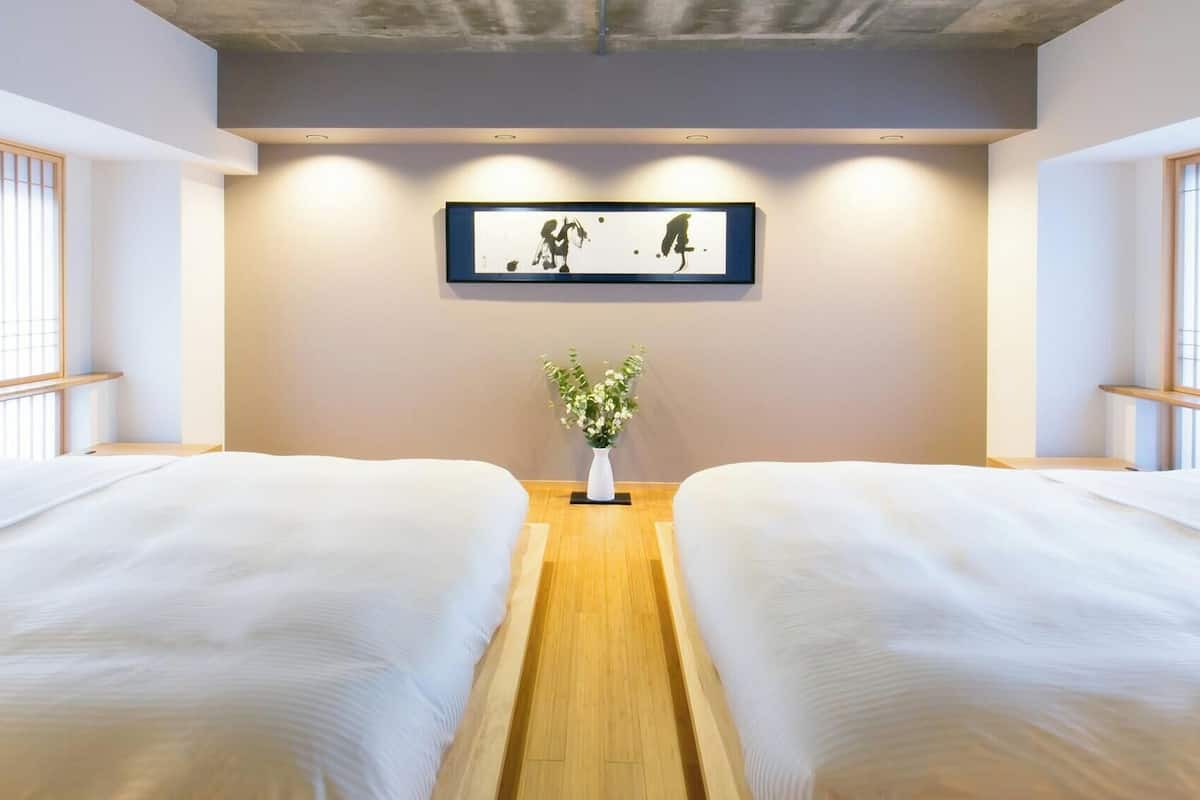 Een hotelkamer met twee bedden, een houten vloer, een ingelijst kunstwerk aan de muur en een kamerplant.