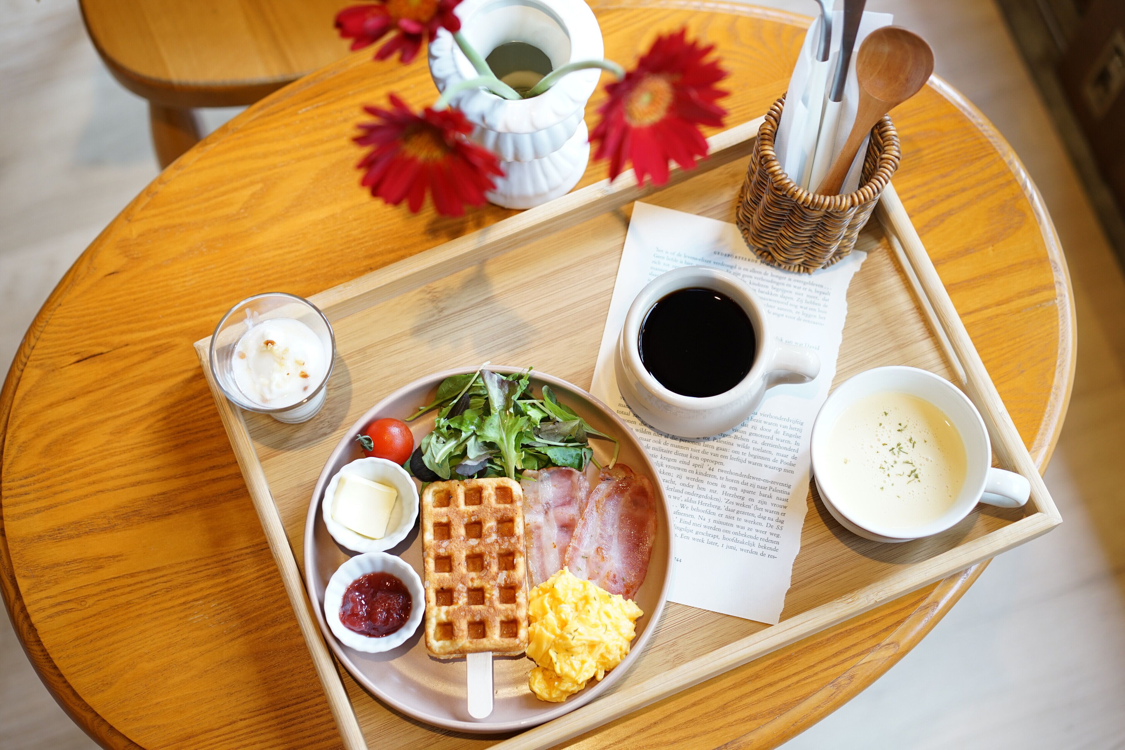 Bandeja de desayuno con waffles, huevos revueltos, tocino y una ensalada sobre una mesa de madera.