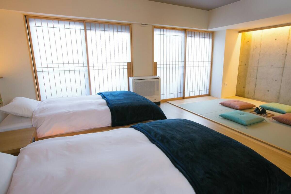 Een hotelkamer met twee bedden, een futon, een verwarming en grote ramen met zonwering.