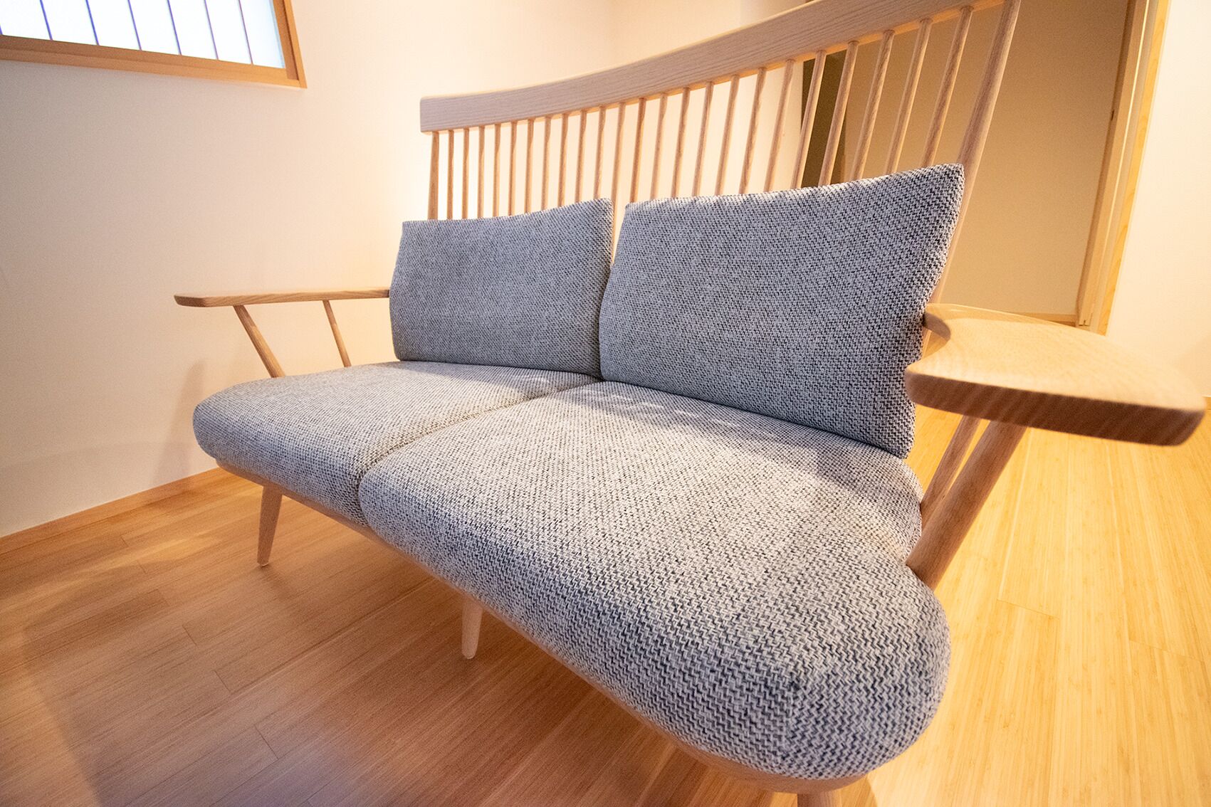 Un divano moderno con una texture intrecciata, gambe in legno e un poggiatesta in legno.