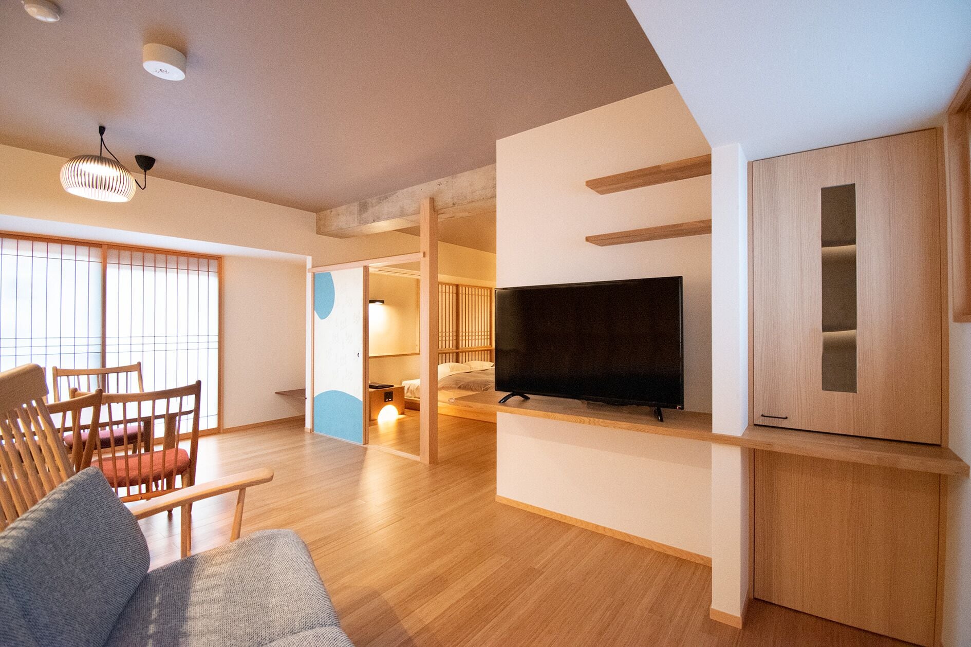 A modern living room with a flat-screen TV, wooden furniture, and a sliding door leading to a bedroom.